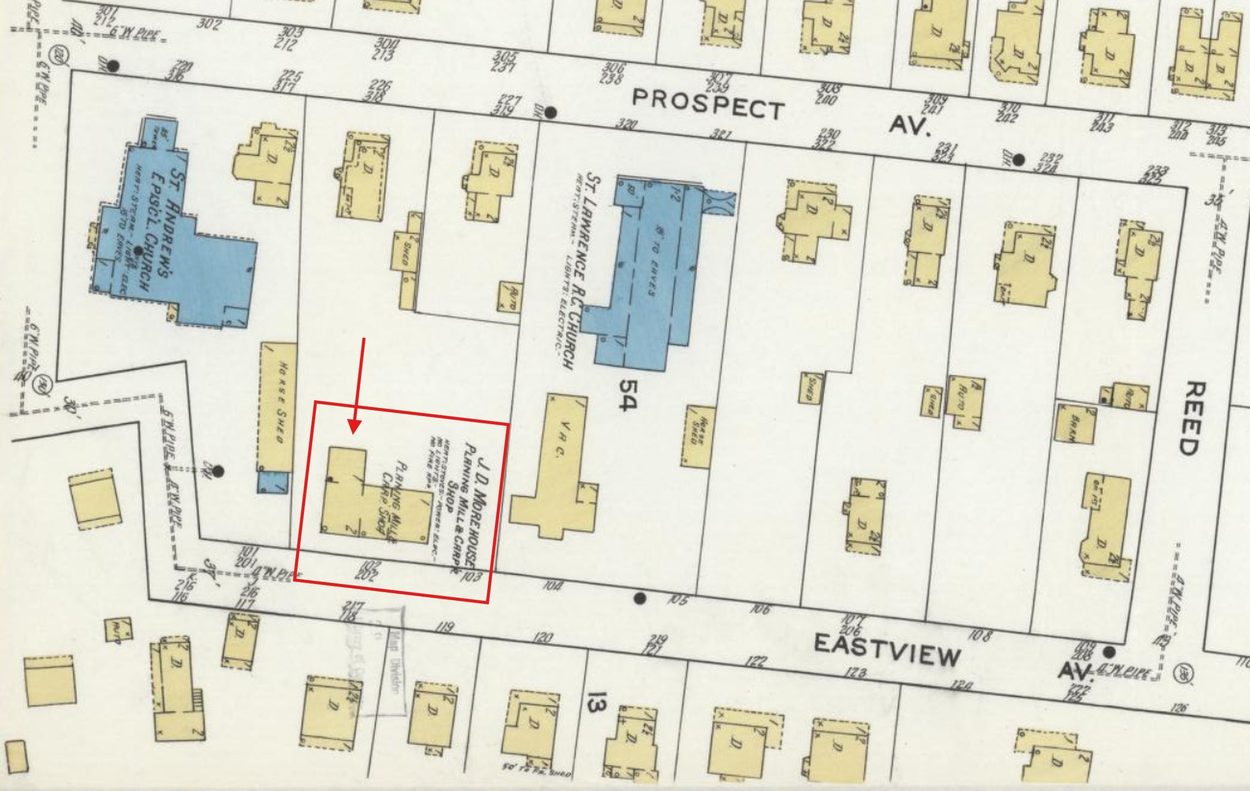 Detail of a color Sanborn fire-insurance map showing a block of the Village of Brewster. Building footprints are shaded yellow for wood-frame and blue for masonry. Streets are labeled Prospect Av., Eastview Av., and Reed. St. Andrew's Episcopal Church and St. Lawrence R.C. Church are labeled in blue. A large yellow L-shaped footprint on the south side of Eastview Avenue is labeled 'J. D. Morehouse Planing Mill & Carp. Shop'; it is highlighted with a red rectangular outline and a red arrow added by the researcher.