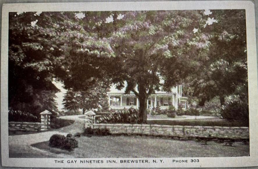 Vintage postcard, black-and-white, showing the Gay Nineties Inn building behind a stone wall and gate posts, large tree shading the front. Caption reads "THE GAY NINETIES INN, BREWSTER, N.Y. PHONE 303."