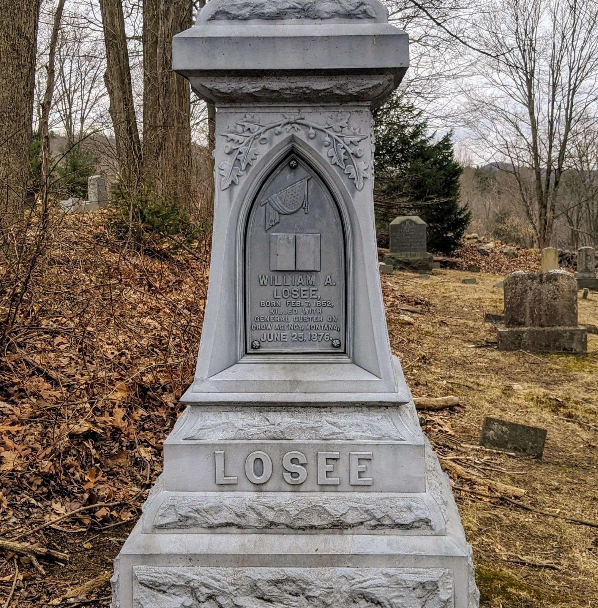 Photograph of the William A. Losee panel on the family monument, showing decorative carved oak leaves and a flag motif. Inscription: WILLIAM A. LOSEE, BORN FEB. 7, 1852, KILLED WITH GENERAL CUSTER ON CROW AGENCY, MONTANA, JUNE 25, 1876. Below, the carved LOSEE base.