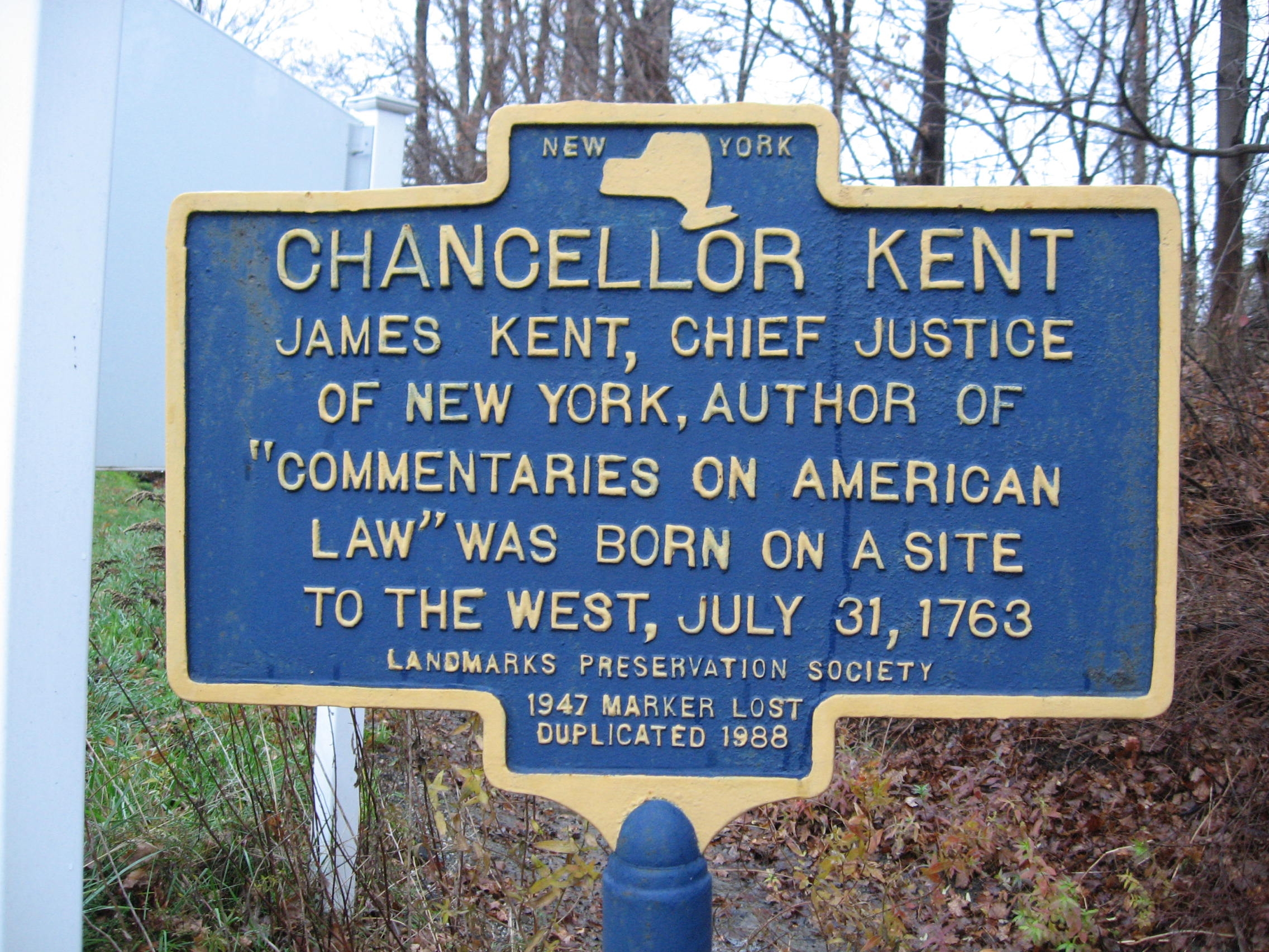 Blue and yellow New York State-style historic marker reading CHANCELLOR KENT: James Kent, Chief Justice of New York, author of 'Commentaries on American Law' was born on a site to the west, July 31, 1763. Landmarks Preservation Society. 1947 Marker Lost, Duplicated 1988.