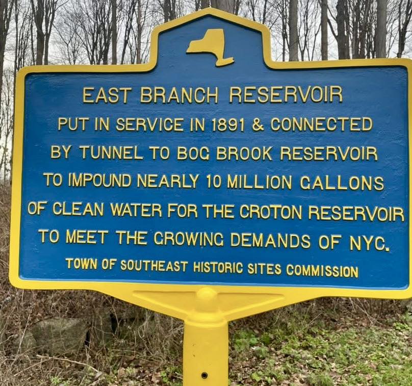 Blue and yellow New York State historic marker for the East Branch Reservoir, reading: Put in service in 1891 & connected by tunnel to Bog Brook Reservoir to impound nearly 10 million gallons of clean water for the Croton Reservoir to meet the growing demands of NYC.