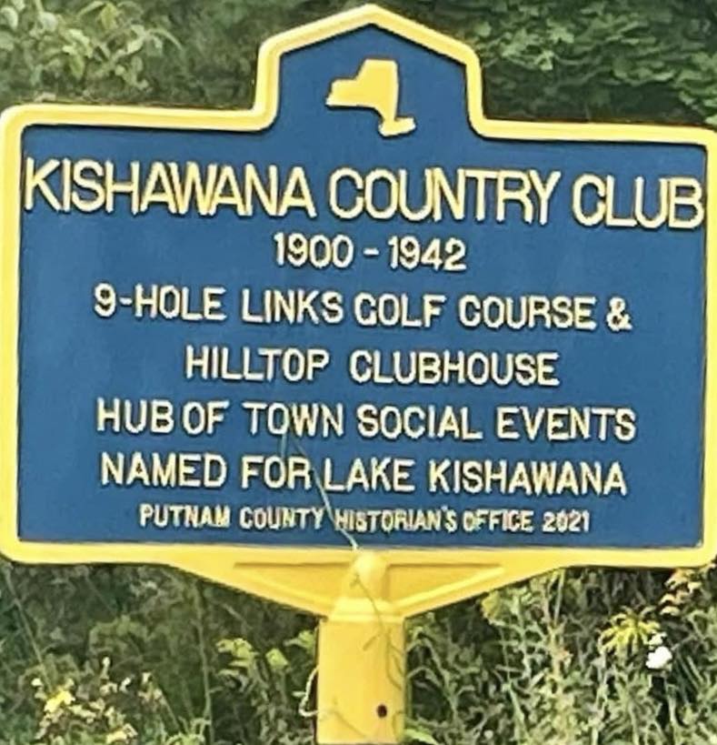 Blue and yellow New York State-style historic marker reading KISHAWANA COUNTRY CLUB, 1900-1942, 9-HOLE LINKS GOLF COURSE & HILLTOP CLUBHOUSE, HUB OF TOWN SOCIAL EVENTS, NAMED FOR LAKE KISHAWANA. Erected by the Putnam County Historian's Office in 2021.