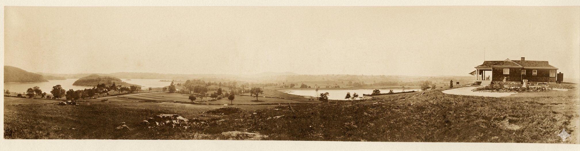 Sepia-toned panoramic view of the Kishawana Country Club setting: the shingled hilltop clubhouse at far right with a deep covered porch, golf course fairways and rolling pastureland in the middle distance, and a body of water at left with a wooded island and farms beyond.