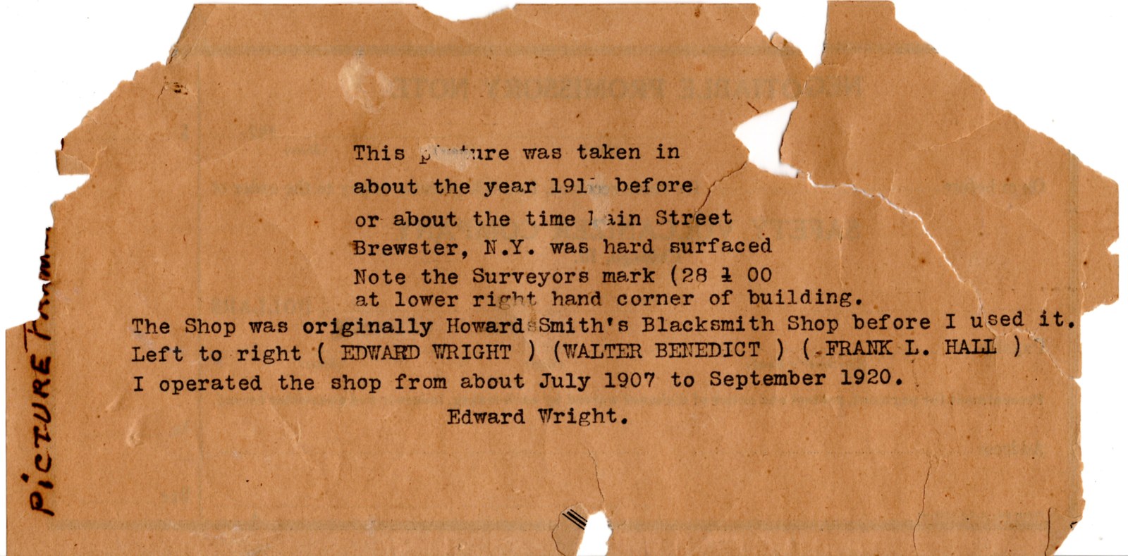 Torn, browned scrap of paper with a typewritten caption identifying the photograph, the surveyor's mark, Howard Smith's blacksmith shop, and the three men — Edward Wright, Walter Benedict, Frank L. Hall — signed Edward Wright.
