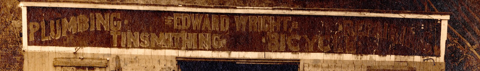 Close crop of the weathered painted sign board: PLUMBING, EDWARD WRIGHT, TINSMITHING, BICYCLES, REPAIRING.