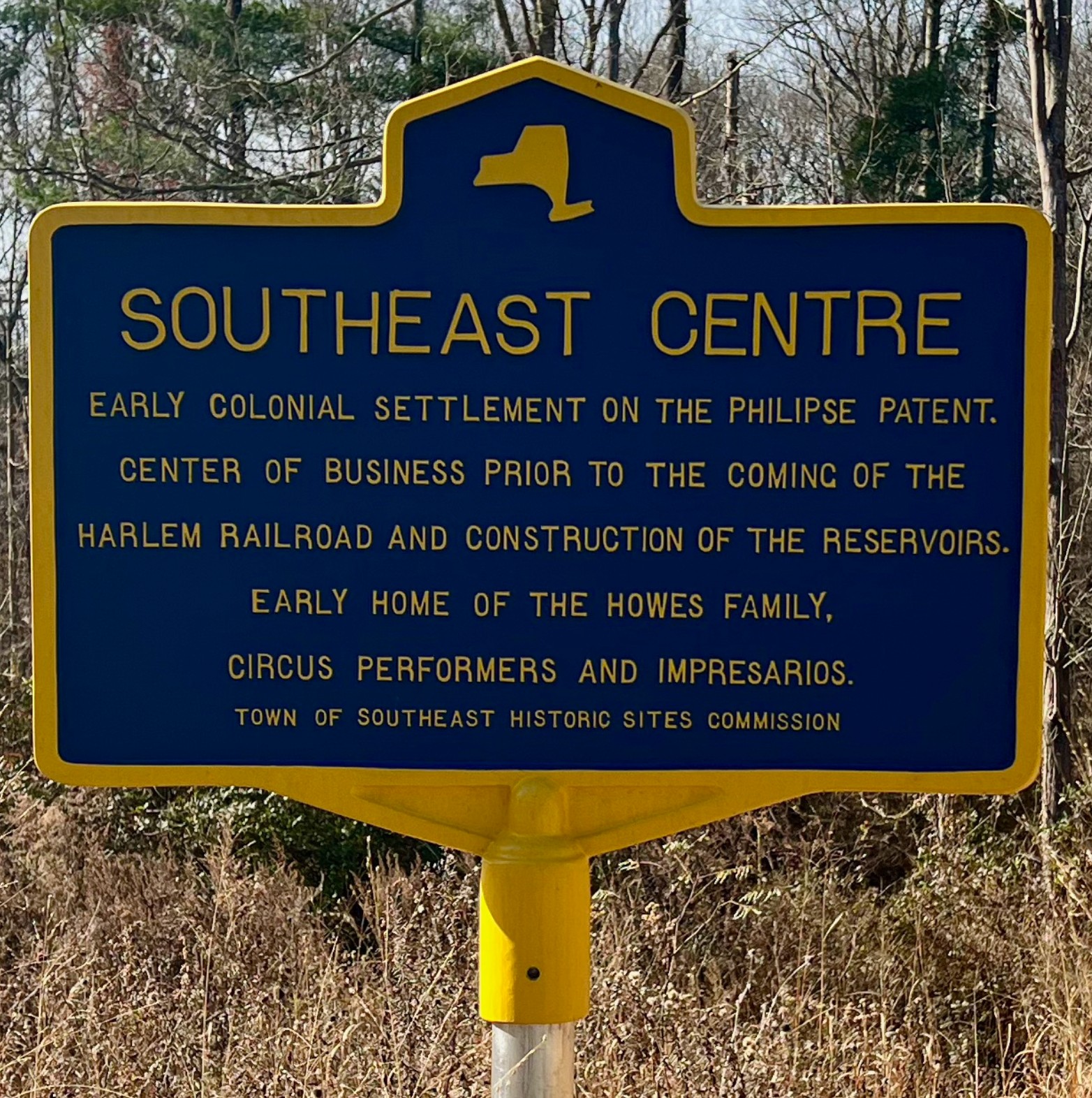 New York State historic marker at Southeast Centre, sponsored by the Town of Southeast Historic Sites Commission. Yellow text on blue background reads: SOUTHEAST CENTRE — Early colonial settlement on the Philipse Patent. Center of business prior to the coming of the Harlem Railroad and construction of the reservoirs. Early home of the Howes Family, circus performers and impresarios.